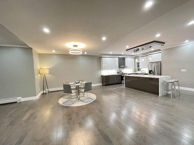 kitchen with wall chimney range hood, dark wood-style floors, a center island, appliances with stainless steel finishes, and light countertops