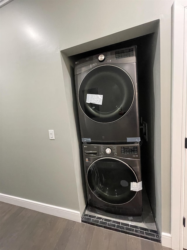 laundry room with laundry area, stacked washer / drying machine, baseboards, and wood finished floors