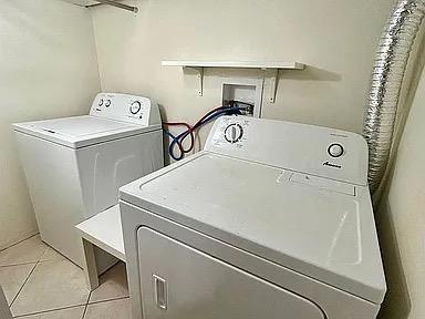 clothes washing area with light tile patterned floors and washer and clothes dryer