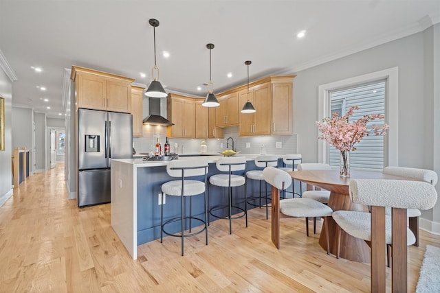 kitchen with wall chimney exhaust hood, stainless steel fridge with ice dispenser, hanging light fixtures, and light brown cabinets