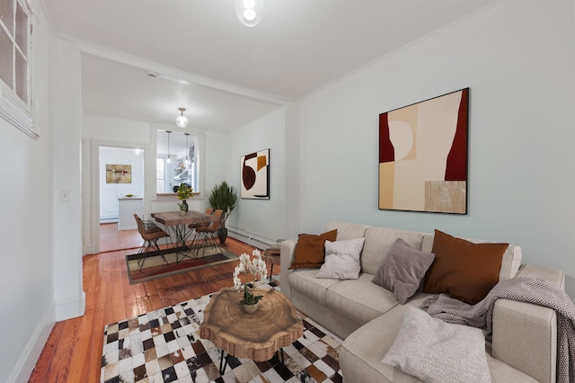 living area with a baseboard heating unit, light wood-style floors, baseboards, and ornamental molding