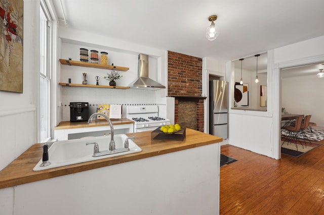 kitchen featuring wall chimney exhaust hood, freestanding refrigerator, gas range gas stove, and wooden counters