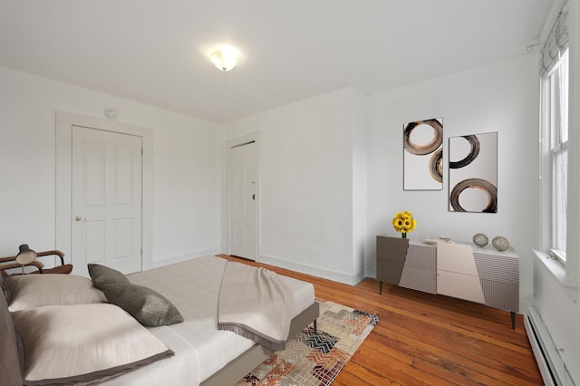 living area featuring a baseboard heating unit, hardwood / wood-style flooring, and baseboards