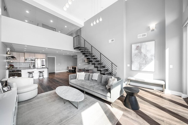 living room featuring visible vents, dark wood-type flooring, stairs, and a towering ceiling