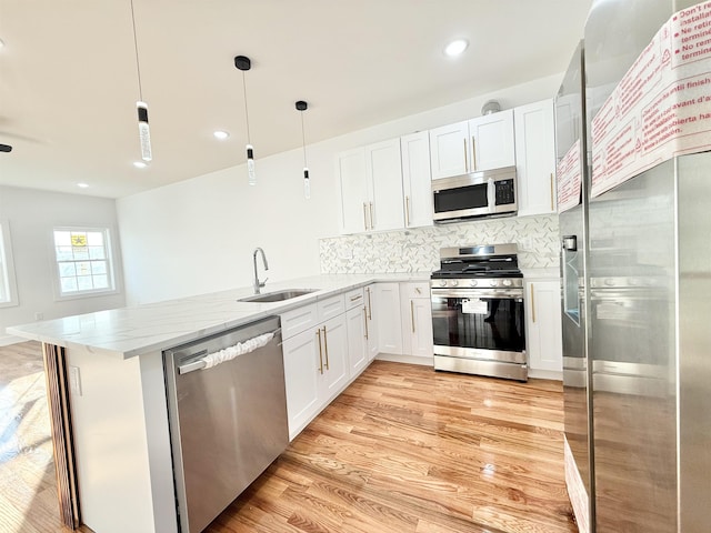 kitchen featuring appliances with stainless steel finishes, white cabinets, a sink, and pendant lighting