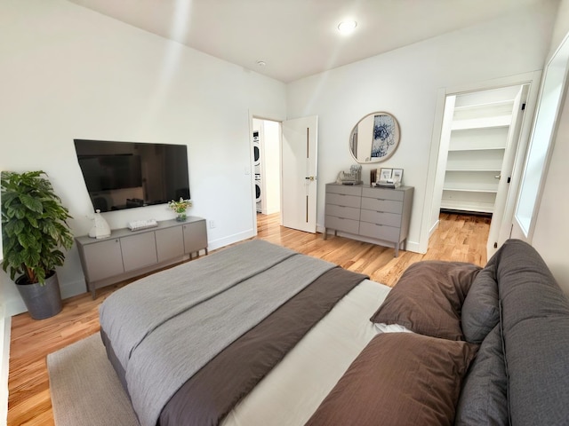 bedroom with a spacious closet, light wood-type flooring, stacked washer and clothes dryer, and baseboards