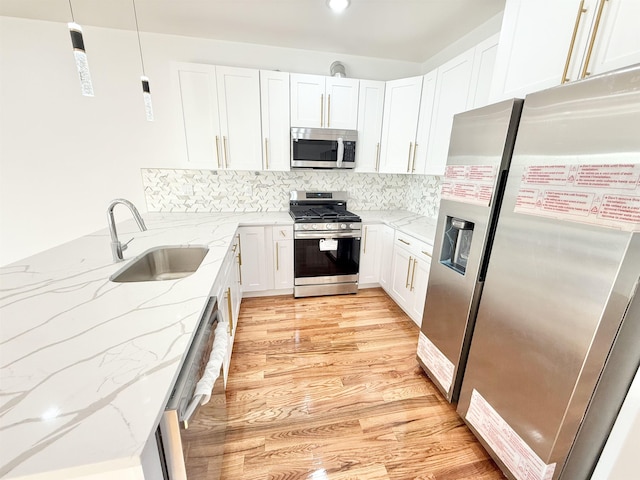 kitchen with white cabinets, light stone counters, hanging light fixtures, stainless steel appliances, and a sink