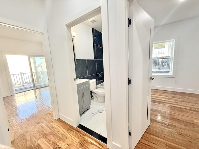 corridor featuring visible vents, a healthy amount of sunlight, light wood-style flooring, and tile walls