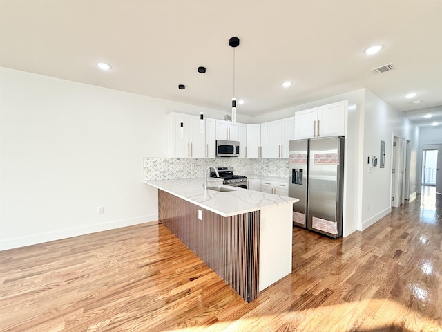 kitchen with decorative backsplash, white cabinets, light stone counters, a peninsula, and stainless steel appliances