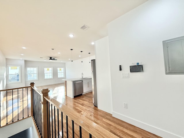 hall with light wood finished floors, visible vents, a sink, an upstairs landing, and electric panel