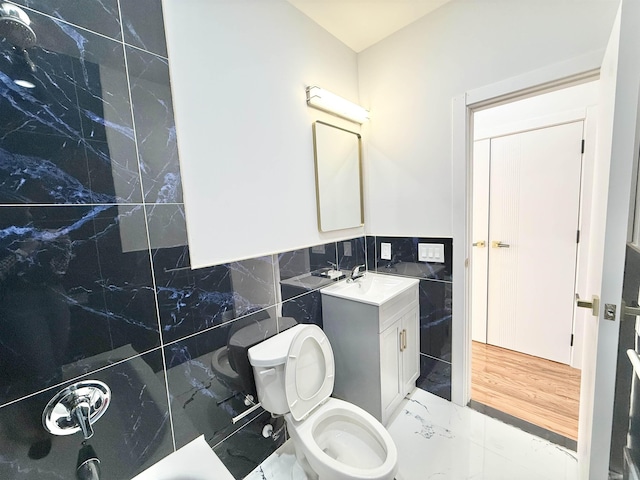 bathroom with toilet, marble finish floor, vanity, and tile walls