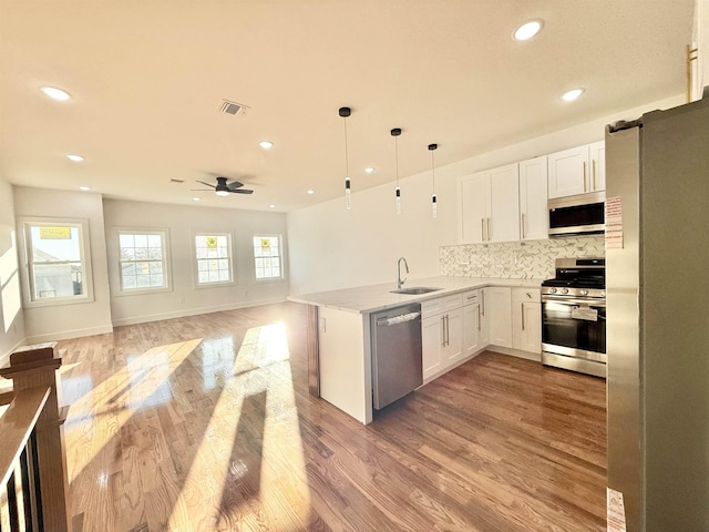 kitchen featuring appliances with stainless steel finishes, open floor plan, white cabinetry, pendant lighting, and a sink