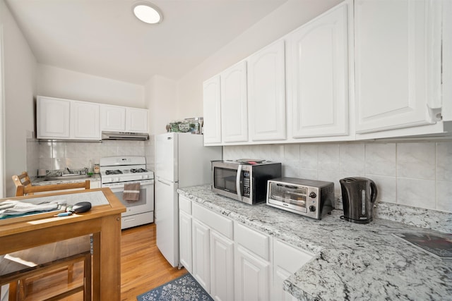 kitchen with white appliances, light stone countertops, light hardwood / wood-style floors, and white cabinets