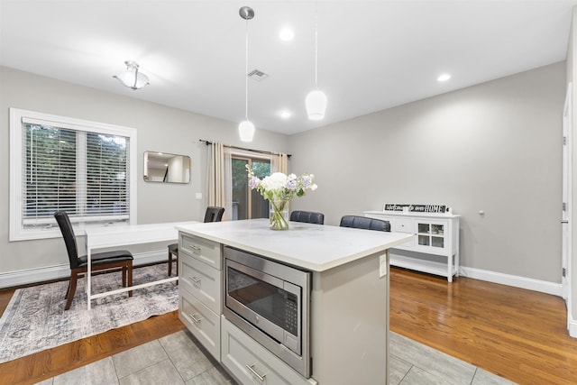 405 Commercial Ave, Cliffside Park, NJ 07010 - kitchen with stainless steel microwave, light countertops, pendant lighting, a center island, and light wood-style floors