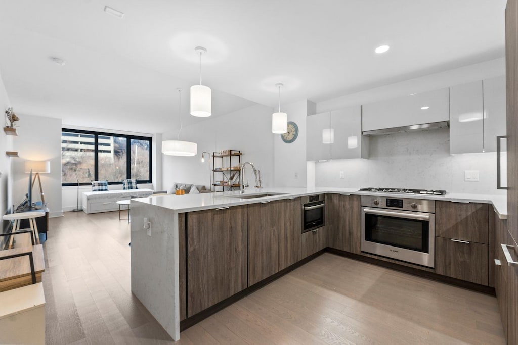 kitchen featuring light wood-type flooring, stainless steel appliances, sink, white cabinets, and hanging light fixtures