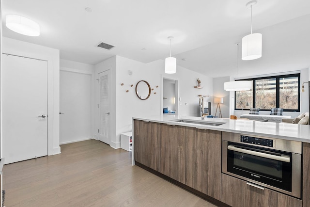 kitchen with decorative light fixtures, oven, light hardwood / wood-style floors, and sink