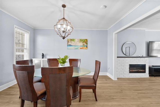 dining space with light wood-style flooring, a notable chandelier, a fireplace, baseboards, and ornamental molding