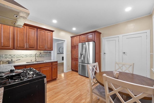 kitchen with tasteful backsplash, black range with gas cooktop, a sink, light wood-type flooring, and stainless steel fridge