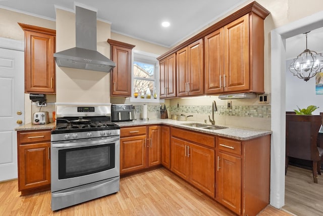 kitchen featuring wall chimney exhaust hood, stainless steel range with gas stovetop, backsplash, light wood-style floors, and a sink