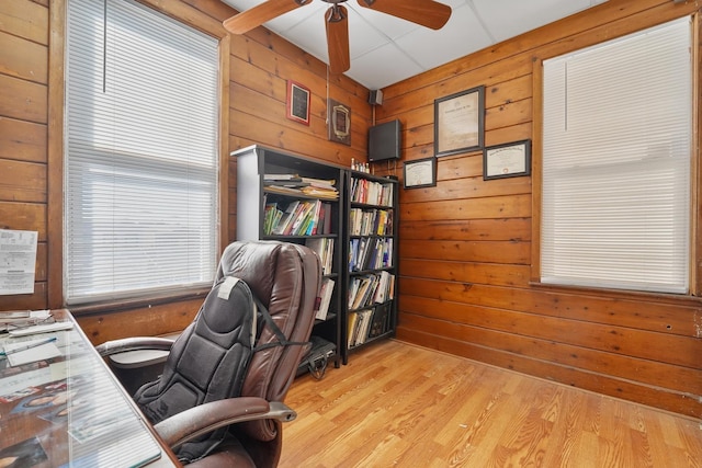 home office featuring light wood-style floors, wood walls, and a ceiling fan