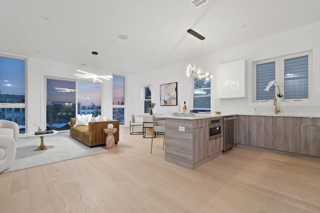 kitchen with ceiling fan with notable chandelier, pendant lighting, dishwasher, light wood-type flooring, and a breakfast bar