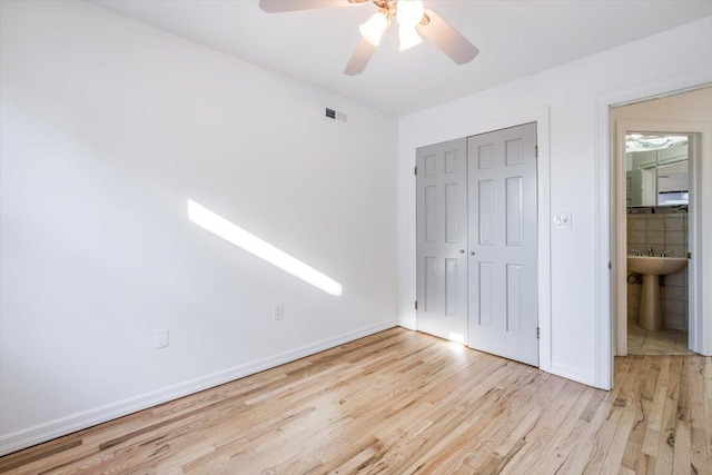 unfurnished bedroom with sink, ensuite bathroom, ceiling fan, light wood-type flooring, and a closet