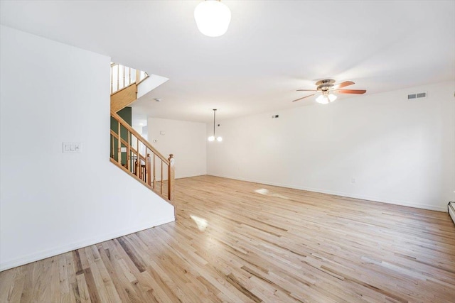 unfurnished room with ceiling fan with notable chandelier and light hardwood / wood-style flooring