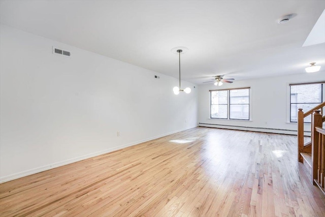 empty room with ceiling fan with notable chandelier, a baseboard heating unit, and light wood-type flooring