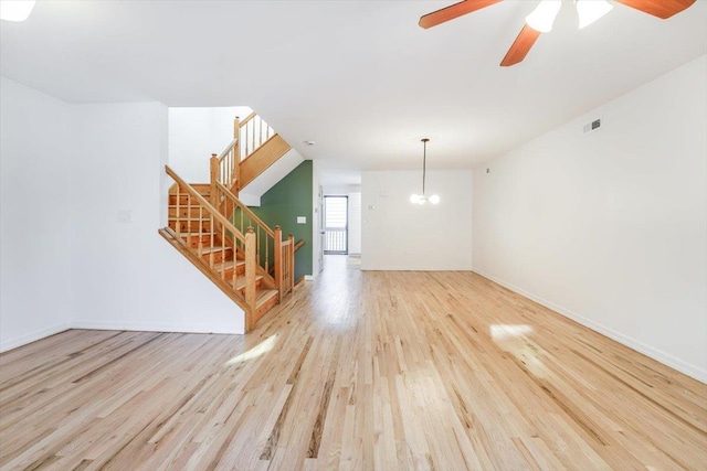 unfurnished living room featuring ceiling fan with notable chandelier and light hardwood / wood-style floors