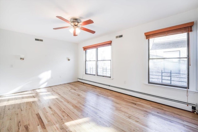 spare room featuring a healthy amount of sunlight, baseboard heating, light wood-type flooring, and ceiling fan