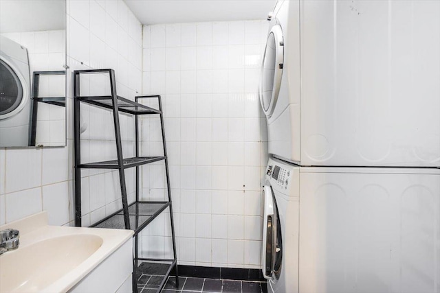 washroom featuring sink, dark tile patterned flooring, tile walls, and stacked washer / dryer