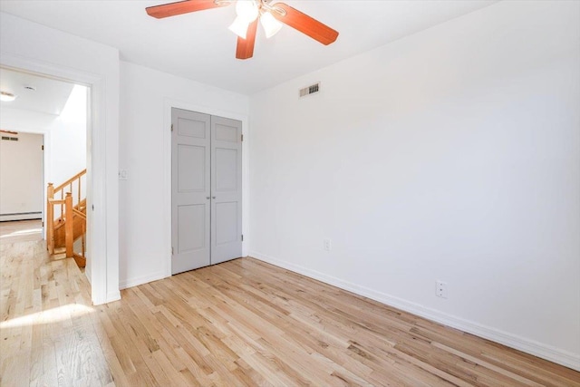 unfurnished bedroom featuring ceiling fan, light wood-type flooring, a closet, and a baseboard heating unit