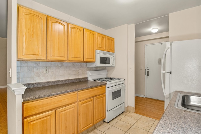 kitchen featuring backsplash, dark countertops, light tile patterned floors, a sink, and white appliances