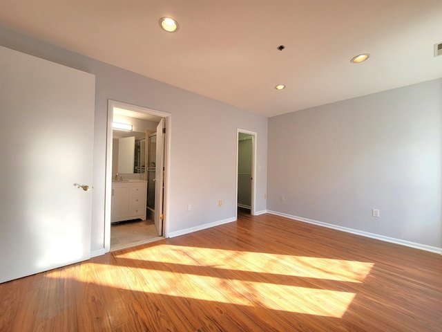 unfurnished bedroom featuring light wood-style floors, recessed lighting, a walk in closet, and baseboards