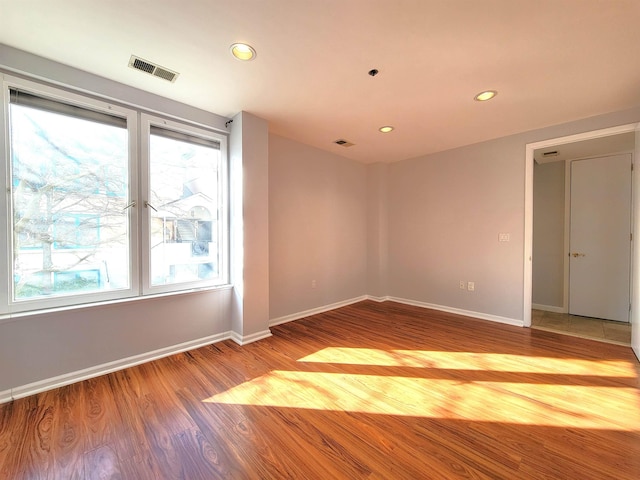 spare room featuring a healthy amount of sunlight, baseboards, visible vents, and wood finished floors