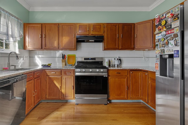 kitchen featuring appliances with stainless steel finishes, tasteful backsplash, a sink, light wood finished floors, and under cabinet range hood