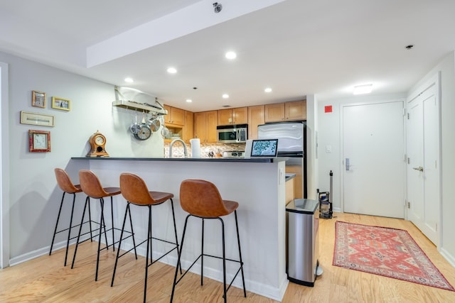 700 1st St Unit 11M, Hoboken, NJ 07030 - kitchen featuring appliances with stainless steel finishes, a peninsula, a kitchen bar, light wood-type flooring, and tasteful backsplash