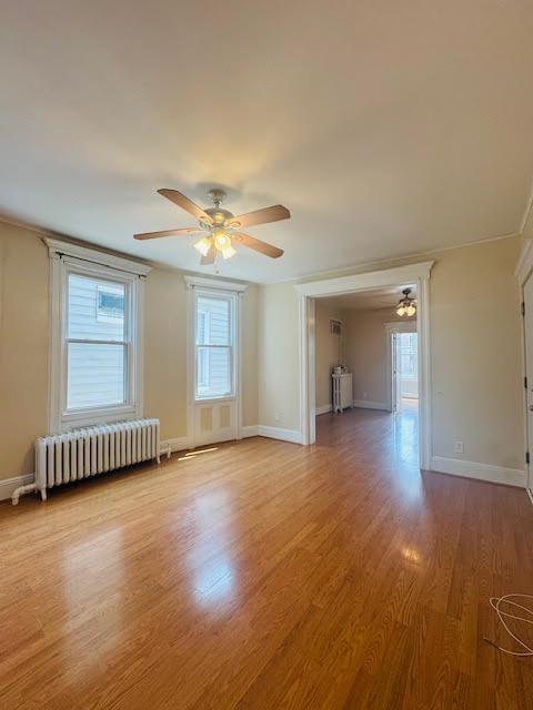 57 W 5th St, Bayonne, NJ 07002 - unfurnished living room featuring radiator, ceiling fan, healthy amount of natural light, and light wood finished floors