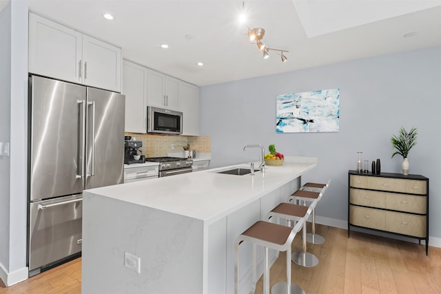 kitchen featuring premium appliances, light countertops, decorative backsplash, white cabinets, and a sink