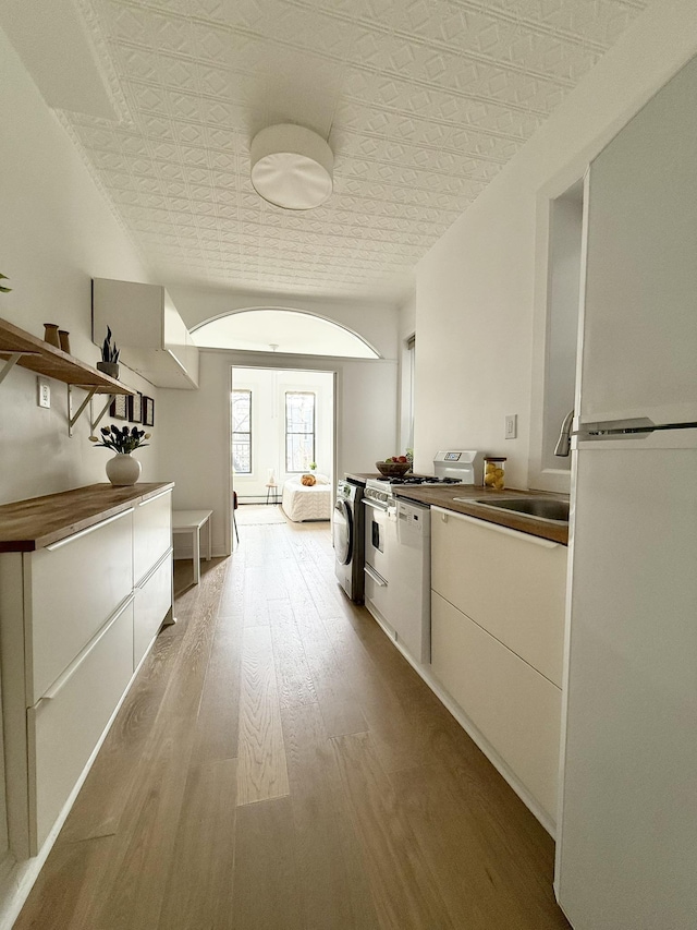 interior space with white appliances, washer / clothes dryer, a sink, light wood finished floors, and an ornate ceiling