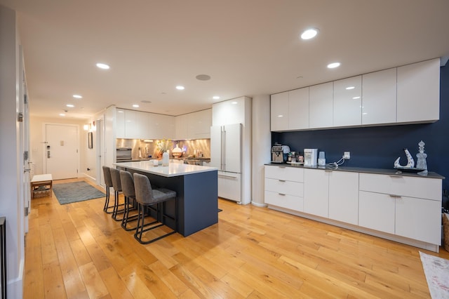 kitchen with a center island, white cabinetry, light hardwood / wood-style floors, high end white refrigerator, and a breakfast bar