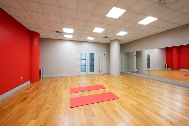 exercise area featuring a paneled ceiling, french doors, and light hardwood / wood-style flooring