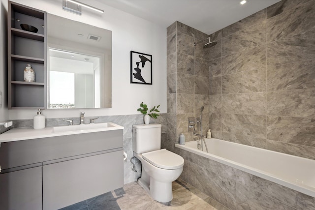 bathroom with tile walls, tiled shower / bath combo, toilet, and vanity