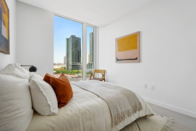 bedroom with a wall of windows, a view of city, wood finished floors, and baseboards