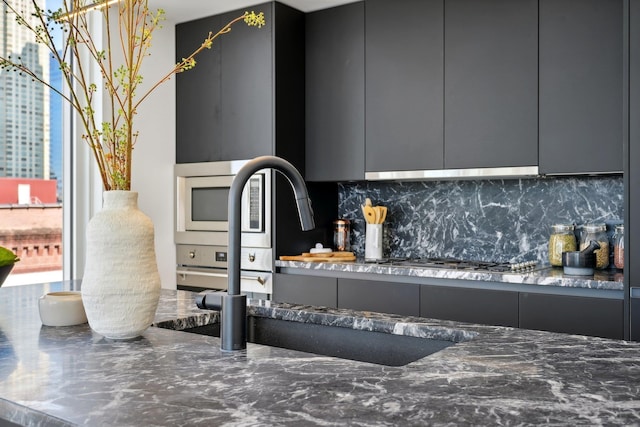 kitchen featuring tasteful backsplash, under cabinet range hood, modern cabinets, gray cabinetry, and stainless steel appliances