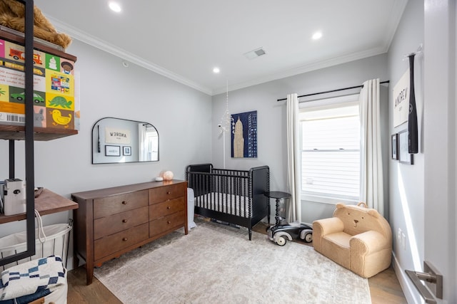 bedroom with hardwood / wood-style flooring, a nursery area, and ornamental molding