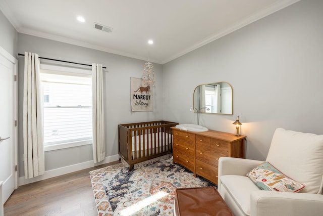 bedroom with a nursery area, light hardwood / wood-style floors, and crown molding