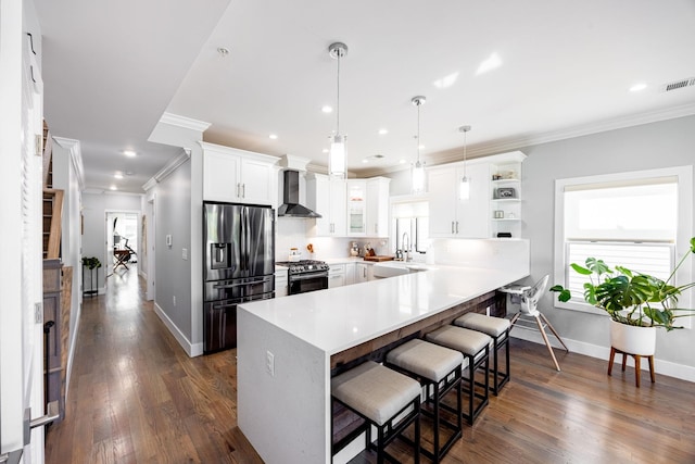 kitchen with stainless steel appliances, dark hardwood / wood-style flooring, white cabinets, wall chimney exhaust hood, and pendant lighting