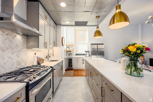 kitchen featuring wall chimney range hood, wine cooler, light countertops, appliances with stainless steel finishes, and a sink