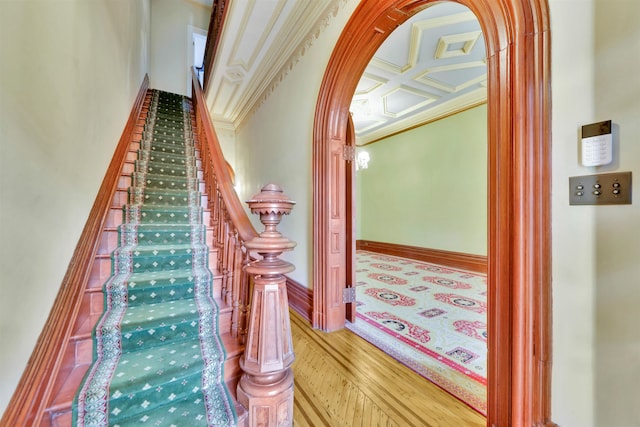 staircase featuring beamed ceiling, wood-type flooring, crown molding, and coffered ceiling